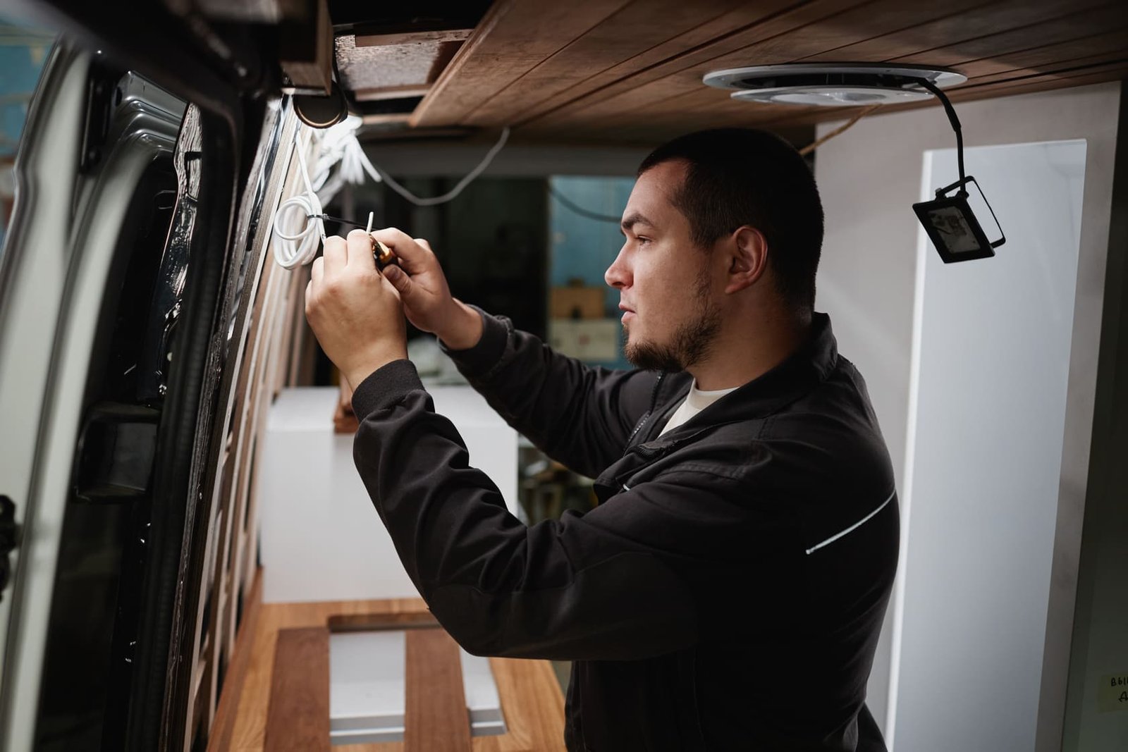 A worker carefully repairs wiring inside a van, similar to how Ozark Grease Pros takes care of grease trap pumping.